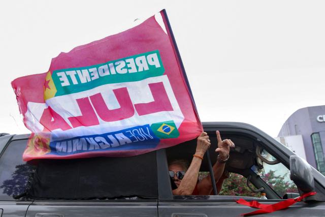 Supporters of Brazil's President and re-election candidate for the leftist Workers' Party (PT) Luiz Inacio Lula da Silva display a campaign flag from a car near during the presidential election in Brasilia on October 4, 2026. Brazilians head to the polls in a highly polarized presidential election between incumbent leftist President Luiz Inacio Lula da Silva -seeking a fourth presidential mandate- and right-wing senator Flavio Bolsonaro, who emerged as the leading figure of the conservative movement following the conviction and imprisonment of his father, former president Jair Bolsonaro. (Photo by Igo Estrela / AFP)