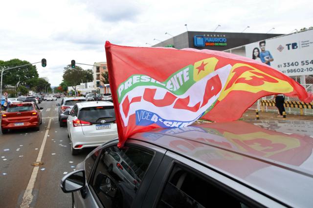 Supporters of Brazil's President and re-election candidate for the leftist Workers' Party (PT) Luiz Inacio Lula da Silva display a campaign flag from a car near during the presidential election in Brasilia on October 4, 2026. Brazilians head to the polls in a highly polarized presidential election between incumbent leftist President Luiz Inacio Lula da Silva -seeking a fourth presidential mandate- and right-wing senator Flavio Bolsonaro, who emerged as the leading figure of the conservative movement following the conviction and imprisonment of his father, former president Jair Bolsonaro. (Photo by Igo Estrela / AFP)