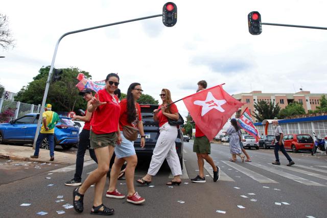 Supporters of Brazil's President and re-election candidate for the leftist Workers' Party (PT) Luiz Inacio Lula da Silva cross a street carrying campaign flags during the presidential election in Brasilia on October 4, 2026. Brazilians head to the polls in a highly polarized presidential election between incumbent leftist President Luiz Inacio Lula da Silva -seeking a fourth presidential mandate- and right-wing senator Flavio Bolsonaro, who emerged as the leading figure of the conservative movement following the conviction and imprisonment of his father, former president Jair Bolsonaro. (Photo by Igo Estrela / AFP)