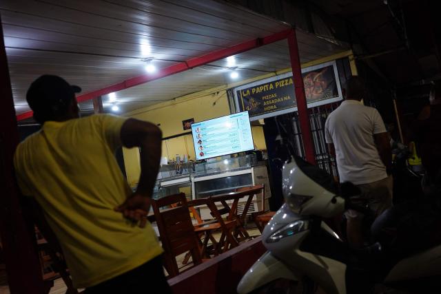People wacth a TV following the partial results of the presidential election in Tabatinga, Amazonas state, Brazil, on October 4, 2026. Brazilian senator Flavio Bolsonaro, son of the far-right former president Jair Bolsonaro, is leading incumbent Luiz Inacio Lula da Silva in partial results from October 4, 2026, election. (Photo by Pablo VERA / AFP)