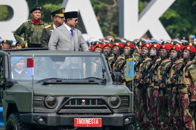 Indonesia's President Prabowo Subianto (R) and Indonesian Armd Forces Commander General Agus Subiyanto (C), stand in an open ceremonial vehicle labeled 'INDONESIA 1' to review the ranks during the 81st Indonesian National Armed Forces Day Parade in Cilangkap, East Jakarta, on October 5, 2026. (Photo by BAY ISMOYO / AFP)