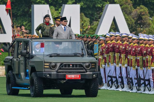 Indonesia's President Prabowo Subianto (R) and Indonesian Armd Forces Commander General Agus Subiyanto (C), stand in an open ceremonial vehicle labeled 'INDONESIA 1' to review the ranks during the 81st Indonesian National Armed Forces Day Parade in Cilangkap, East Jakarta, on October 5, 2026. (Photo by BAY ISMOYO / AFP)