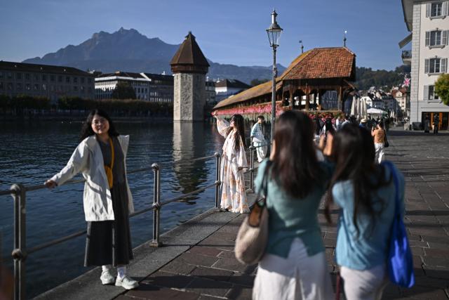 Asian tourists pose for a photograph in front of Lucerne’s iconic Kapellbrьcke, also known in English as the Chapel Bridge, in Lucerne, central Switzerland, on October 4, 2026. Switzerland’s most popular tourist destinations are facing growing pressure from mass tourism, as increasing numbers of visitors crowd iconic Alpine resorts. (Photo by Fabrice COFFRINI / AFP)