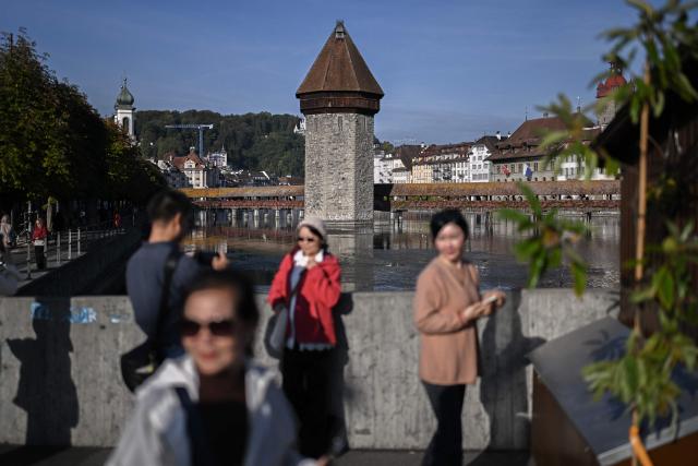 Asian tourists pose for a photograph in front of Lucerne’s iconic Kapellbrьcke, also known in English as the Chapel Bridge, in Lucerne, central Switzerland, on October 4, 2026. Switzerland’s most popular tourist destinations are facing growing pressure from mass tourism, as increasing numbers of visitors crowd iconic Alpine resorts. (Photo by Fabrice COFFRINI / AFP)