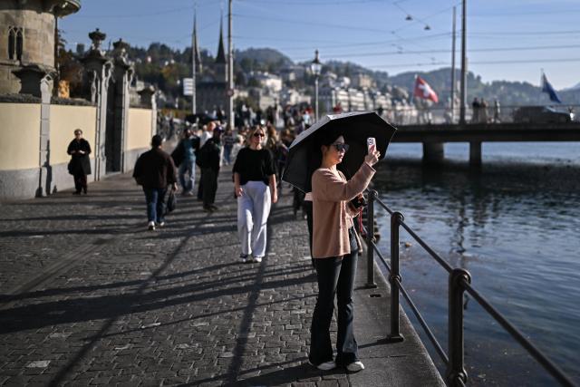 A tourist takes a photograph in Lucerne, on the shores of Lake Lucerne, in central Switzerland, on October 4, 2026. Switzerland’s most popular tourist destinations are facing growing pressure from mass tourism, as increasing numbers of visitors crowd iconic Alpine resorts. (Photo by Fabrice COFFRINI / AFP)