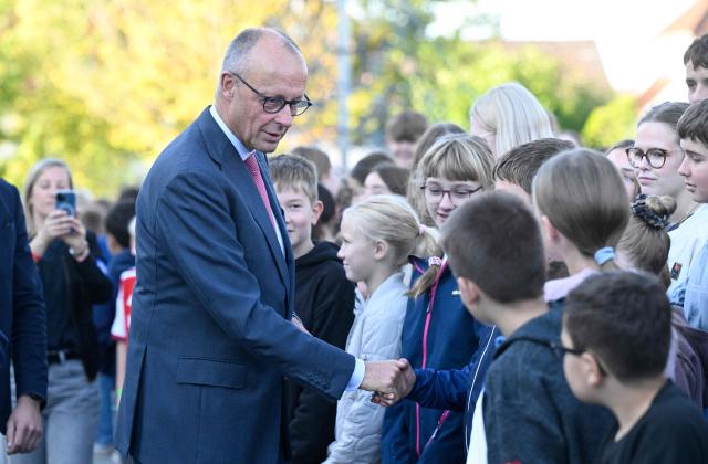 German Chancellor Friedrich Merz shakes hands with young students as he arrives for a visit at his former secondary school, the Friedrich-Spee-Gymnasium in Ruethen, western Germany, on October 5, 2026, as the school is celebrating its 100th anniversary. (Photo by INA FASSBENDER / AFP)
