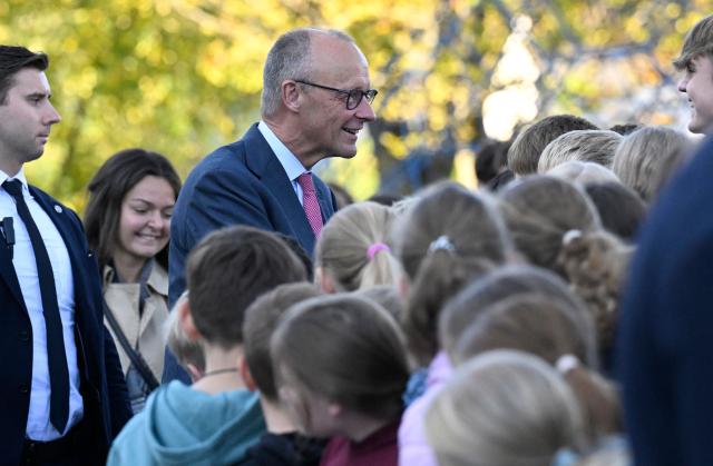 German Chancellor Friedrich Merz (C) talks with young students as he arrives for a visit at his former secondary school, the Friedrich-Spee-Gymnasium in Ruethen, western Germany, on October 5, 2026, as the school is celebrating its 100th anniversary. (Photo by INA FASSBENDER / AFP)