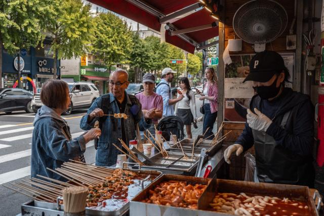 People eat in front of a shop at the Mangwon Market in Seoul on October 5, 2026. (Photo by Philip FONG / AFP)
