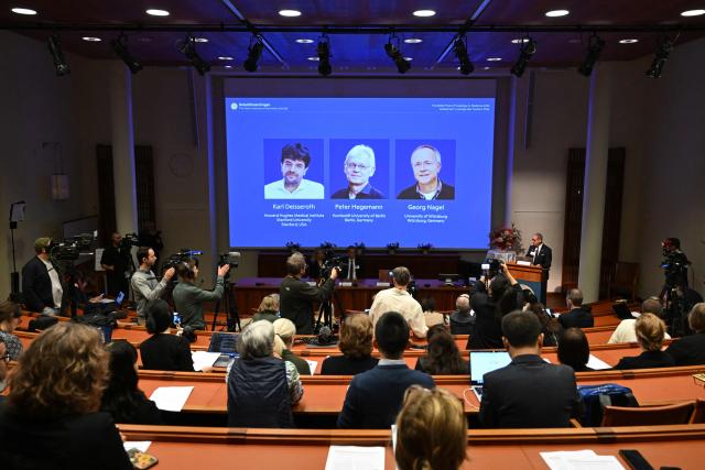 Karolinska Institute neuroscience professor Abdel El Manira (R) speaks in front of a screen displaying portraits of (L-R) US scientist Karl Deisseroth and German scientists Peter Hegemann and Georg Nagel during the announcement of the winners of the 2026 Nobel Prize in Physiology or Medicine at the Karolinska Institute in Stockholm, Sweden, on October 5, 2026. US scientist Karl Deisseroth and German scientists Peter Hegemann and Georg Nagel share the 2026 Nobel Prize in Physiology or Medicine for their discoveries concerning light-gated ion channels and optogenetics. (Photo by Jonathan Nackstrand / AFP)
