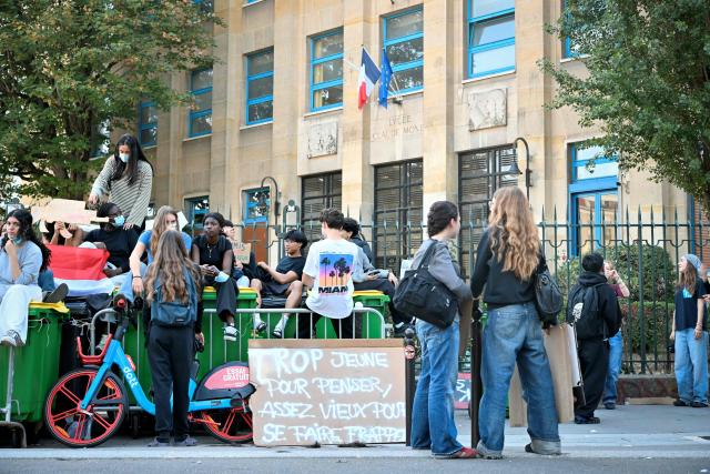 Protesting students gather next to a placard reading "Too young to think, old enough to get beaten up" as they carry out a blockading action at the Claude Monet secondary school, in Paris, on October 5, 2026. The start of a "black week"? Hundreds of high schools are going to close again, at least partially, on October 5, 2026, on the eve of a new day of mobilisation, which unions are calling on people to join, and as calls for a hard blockade are flourishing on social media as students demand more resources for their schools and denouncce the unsanitary state of buildings, overcrowded classes, or unreplaced absences, particularly in working-class neighbourhoods, or even the inequalities created by Parcoursup. (Photo by LOU BENOIST / AFP)