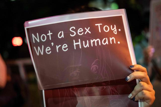 A woman holds up a placard reading 'Not a Sex Toy. We're Human' during a protest against the killing of a woman in Okinawa allegedly committed by a US Marine Corps member, in front of the Prime Minister's Office in Tokyo on October 5, 2026. A woman's murder allegedly committed by a US Marine in Okinawa is a "heinous crime", Japan's premier said on October 5, as the new accusation of violence involving American forces sparked public outrage. (Photo by Yuichi YAMAZAKI / AFP)