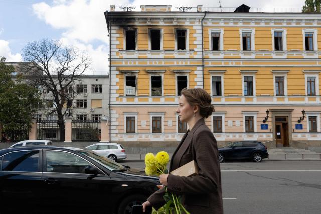 A girl carries yellow flowers as she walks past the damaged building of the National Academy of Sciences of Ukraine in Kyiv on October 5, 2026, amid the Russian invasion of Ukraine. (Photo by Tetiana DZHAFAROVA / AFP)