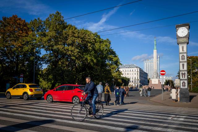 This photograph taken on October 4, 2026, shows passers-by crossing Rainis Boulevards next to the Freedom Monument (Brivibas Piemineklis) in Riga, Latvia. (Photo by Wojtek RADWANSKI / AFP)