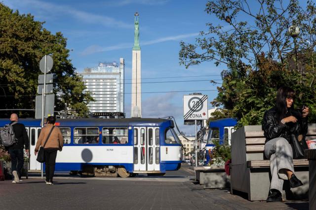 This photograph taken on October 4, 2026, shows a woman siting on the bench and passers-by crossing Rainis Boulevards next to the Freedom Monument (Brivibas Piemineklis) in downtown Riga, Latvia. (Photo by Wojtek RADWANSKI / AFP)