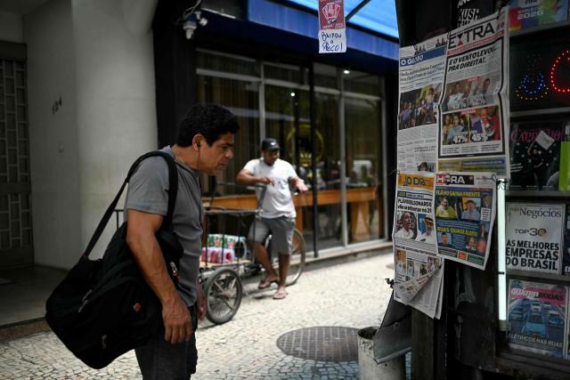 A man looks at wewspapers displaying coverage of Brazil's presidential election results at a newsstand in Rio de Janeiro, Brazil, on October 5, 2026. The Sao Paulo stock exchange opened sharply higher on October 5 after a surprise first round election result saw right-wing senator Flavio Bolsonaro edge past incumbent Luiz Inacio Lula da Silva. (Photo by MAURO PIMENTEL / AFP)