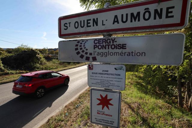A motorist passes by a road sigh for the entrance to the town where 14-year-old student Eden of the Chateau d'Epluches vocational secondary school suffered severe facial injuries from the launch of a tear gas canister during a student protest at the school, in Saint-Ouen-l'Aumone, northwest of Paris, on October 5, 2026. The teenager's parents are preparing to file a complaint and an investigation has already been assigned to the General Inspectorate of the National Police (IGPN). The IGPN has been tasked with six investigations since the start of a high school student protests AFP learned on October 5 from a source familiar with the matter. Since late September, students have blocked the entrances to hundreds of schools, complaining of teacher absences, overloaded timetables, dilapidated classrooms and buildings ill-adapted to rising temperatures, among other grievances. (Photo by Mehdi FEDOUACH / AFP)
