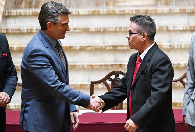 Bolivia's President Rodrigo Paz (L) shakes hands with interim attorney general Jose Armando Urioste during a ceremony recognizing Urioste as the country's interim attorney general at the Government Palace in La Paz on October 5, 2026. The Bolivian Congress suspended the attorney general, who was detained after being accused by the United States of alleged links to drug trafficking, and appointed an interim replacement on October 3 following a lengthy emergency session. Roger Mariaca, who had headed the Public Prosecutor's Office from 2024 until his arrest on September 30, will be temporarily replaced by Jose Armando Urioste. (Photo by Aizar RALDES / AFP)