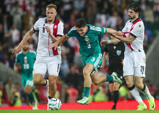 Northern Ireland's midfielder #03 Justin Devenny (C) tuns past Georgia's defender #20 Saba Sazonov (R) during the UEFA Nations League, League B, Group 2 match between Northern Ireland and Georgia at Windsor Park in Belfast, Northern Ireland on October 5, 2026. (Photo by Paul Faith / AFP)