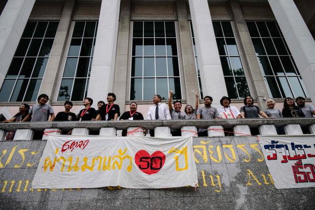 Attendees stand above a banner displayed to mark the 50th anniversary of the Thammasat University massacre on October 6, 1976, during the annual commemoration ceremony for the event at Thammasat University in Bangkok on October 6, 2026. (Photo by ANTHONY WALLACE / AFP)