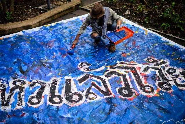 An artist paints a large canvas during an event at Thammasat University in Bangkok on October 6, 2026, to mark the 50th anniversary of the Thammasat University massacre on October 6, 1976. (Photo by ANTHONY WALLACE / AFP)