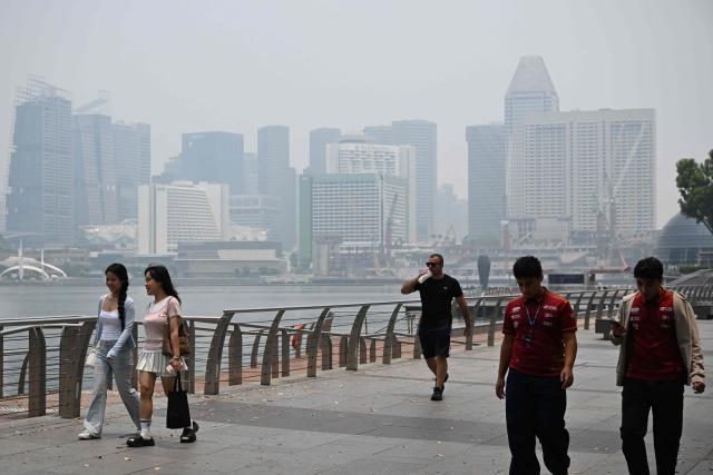 People walk along the boulevard at Marina Bay as buildings are seen shrouded with haze in Singapore on October 6, 2026. Indonesia has been battling fires for weeks in parts of Borneo and Sumatra, sending suffocating haze across the islands and neighbouring Malaysia and Singapore. (Photo by Roslan RAHMAN / AFP)