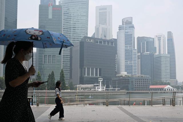 People walk along the boulevard at Marina Bay as buildings are seen shrouded with haze in Singapore on October 6, 2026. Indonesia has been battling fires for weeks in parts of Borneo and Sumatra, sending suffocating haze across the islands and neighbouring Malaysia and Singapore. (Photo by Roslan RAHMAN / AFP)
