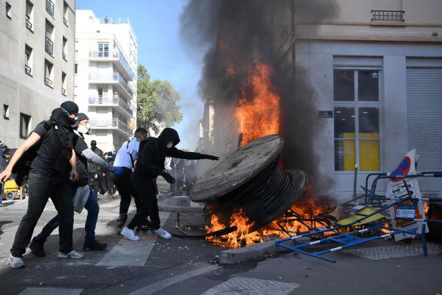 A protester throws a roll of hose into a fire during clashes on the sidelines of a demonstration of high-school students as part of a nationwide protest movement over learning conditions in Lyon, on October 6, 2026. Since late September, pupils have barred the entrances to hundreds of schools, complaining of teacher absences, overloaded timetables, dilapidated classrooms and buildings ill-adapted to rising temperatures, among other grievances. (Photo by Olivier CHASSIGNOLE / AFP)