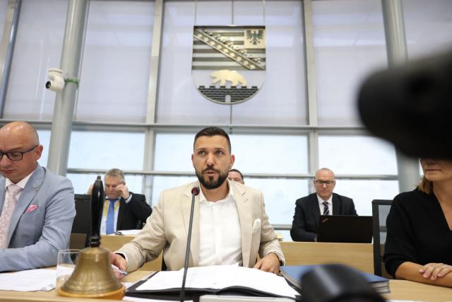 Newly elected state parliament president Tobias Rausch of the far-right Alternative for Germany (AfD) party speaks at the lectern after his election during the first constituent session of the state parliament of Saxony-Anhalt in Magdeburg, eastern Germany, on October 6, 2026. Newly elected state lawmakers gather for the first time in the parliament building in the state capital Magdeburg to elect a speaker, with a candidate of the far-right Alternative for Germany (AfD) expected to win. The AfD is poised to preside over a state assembly for the first time following its landslide election victory in the eastern state of Saxony-Anhalt. The AfD took nearly 44 percent of the vote in the September 2026 state election. (Photo by Jan Woitas / POOL / AFP)
