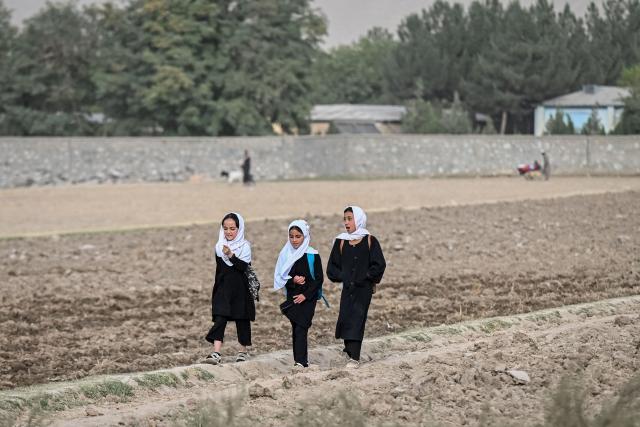 Afghan girls walk across a field after attending school on the outskirts of the Fayzabad district in Afghanistan's Badakhshan province on October 6, 2026. (Photo by Omer ABRAR / AFP)