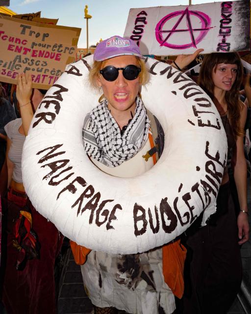 A protester has a buoy around his neck reading "budget disaster" during a demonstration of high-school students as part of a nationwide protest movement over learning conditions in the south-eastern city of Nice, on October 6, 2026. Since late September, pupils have barred the entrances to hundreds of schools, complaining of teacher absences, overloaded timetables, dilapidated classrooms and buildings ill-adapted to rising temperatures, among other grievances. (Photo by Valery HACHE / AFP)