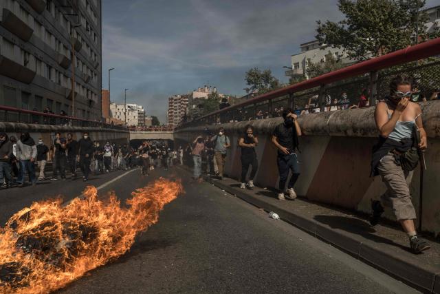 Protesters march along a road past a burning garbage bin during a demonstration of high-school students as part of a nationwide protest movement over learning conditions in Toulouse, on October 6, 2026. Since late September, pupils have barred the entrances to hundreds of schools, complaining of teacher absences, overloaded timetables, dilapidated classrooms and buildings ill-adapted to rising temperatures, among other grievances. (Photo by Ed JONES / AFP)