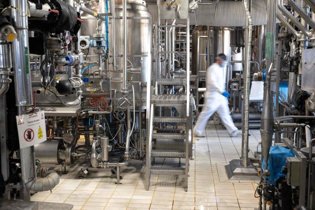 An employee of French industrial cheese producer Bel walks past ovens on the 'La Vache qui rit' (The Laughing Cow) cheese production line during a press visit for the hundred year anniversary of the brand at the Lon-le-Saunier factory, eastern France, on October 6, 2026. (Photo by SEBASTIEN BOZON / AFP)
