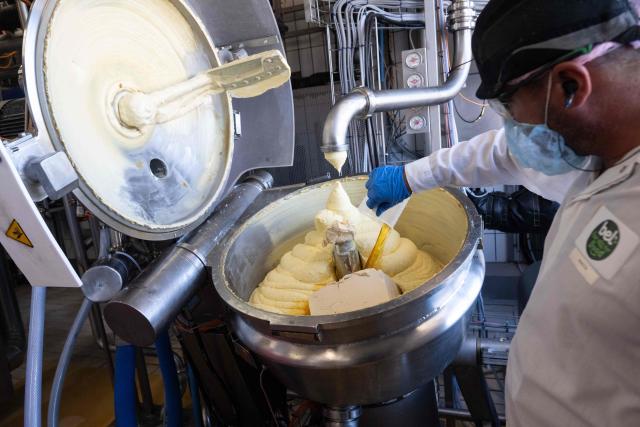 An employee of French industrial cheese producer Bel adds ingredients to a vat on the 'La Vache qui rit' (The Laughing Cow) cheese production line during a press visit for the hundred year anniversary of the brand at the Lon-le-Saunier factory, eastern France, on October 6, 2026. (Photo by SEBASTIEN BOZON / AFP)