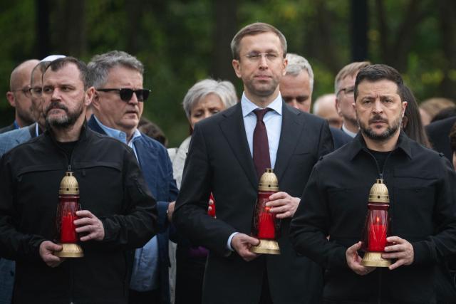 President of Ukraine Volodymyr Zelensky (R), Prime Minister of Ukraine Sergey Koretsky (C) and Secretary of the National Security and Defense Council of Ukraine Igor Klymenko (L) hold candles as they take part in a memorial ceremony at the Babyn Yar National Historical and Memorial Reserve to honor the victims of the mass execution of civilians by the Nazis during World War II, in Kyiv on October 6, 2026, amid the Russian invasion of Ukraine. (Photo by Genya SAVILOV / AFP)