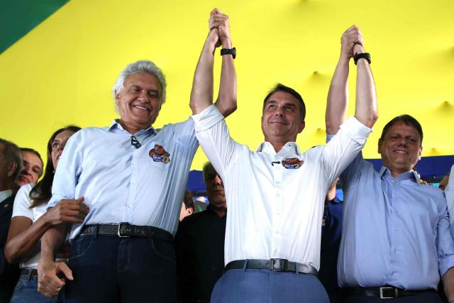 Brazil's right-wing senator and Liberal Party (PL) presidential candidate Flavio Bolsonaro (C) raises hands with former presidential candidate Ronaldo Caiado (L) and Sao Paulo Governor Tarcisio de Freitas during a rally in Goiania, Goias state, Brazil, on October 6, 2026. Right-wing Flavio Bolsonaro heads into Brazil's October 25 presidential runoff in a position of strength and with the backing of US President Donald Trump, while President Luiz Inacio Lula da Silva faces an uphill battle to stage a comeback. (Photo by Sergio LIMA / AFP)