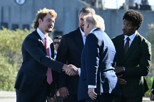 US President Donald Trump is greeted by Baltimore Ravens football players, L/R, Ryan Eckley, Nick Moore, and Marlon Humphrey upon arrival in Sparrows Point, Maryland, ahead of an event at Anduril Industries, on October 6, 2026. Anduril Industries is making an announcement about its future plans at the former Bethlehem Steel location. (Photo by Jim WATSON / AFP)