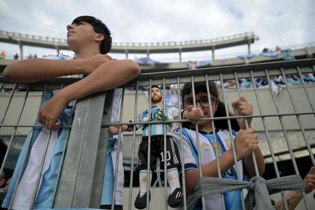 Argentina fans stand behind a barrier with a doll depicting Argentina's forward Lionel Messi ahead of the international friendly football match between Argentina and Benin at the Mas Monumental stadium in Buenos Aires on October 6, 2026. Argentines will bid farewell to Lionel Messi with a huge "thank you" themed send-off in Buenos Aires, where the legendary captain will end his more-than-two-decade international career with a friendly against Benin. (Photo by JUAN MABROMATA / AFP)