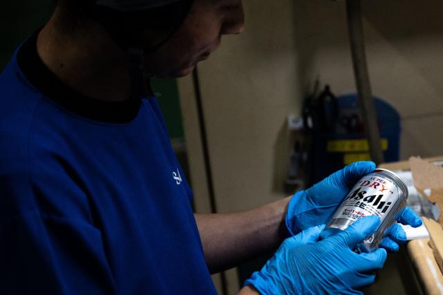 (FILES) A staff member inspects a can of beer at the Asahi Group Holdings' Ibaraki Brewery, which produces around 5.9 million cans of beer daily, during a media tour of the facility in Moriya city, Ibaraki Prefecture on September 7, 2026. Japanese authorities raided four major beer manufacturers October 7, 2026 over suspicions they colluded to hike beverage prices in a violation of anti-monopoly laws, a source familiar with the matter and the firms said. (Photo by Philip FONG / AFP)