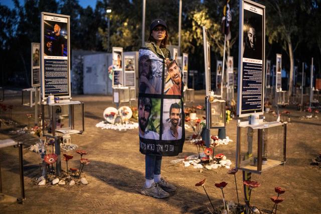 A mourner holds a poster with portraits of victims while standing at the site of the Nova music festival in Re'im, southern Israel on October 7, 2026, to mark the third anniversary of Hamas's October 7, 2023 attack. Mourners observed a moment of silence on October 7 at sites in southern Israel attacked by Hamas three years earlier, the country's deadliest ever attack which triggered a massive Israeli offensive in Gaza. At the site of the Nova music festival, which Hamas militants infiltrated on October 7, 2023 through cars and paragliders, family members bowed their heads at 6:29 am (0329 GMT), surrounded by portraits of victims with flowers placed underneath. (Photo by JOHN WESSELS / AFP)