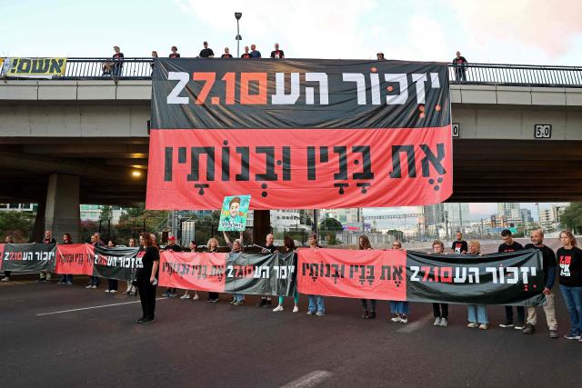 Israelis hold banners reading 'Remember and never forget' as they block the highway to conduct a moment of silence as part of a memorial ceremony in Tel Aviv on October 7, 2026, to mark the third anniversary of Hamas's October 7 attack. Israel marked the third anniversary of Hamas's October 7 attack with silent tributes, new strikes on Gaza and intense political debate, weeks before elections in which the country's deadliest day will be front and centre. (Photo by Jack GUEZ / AFP)