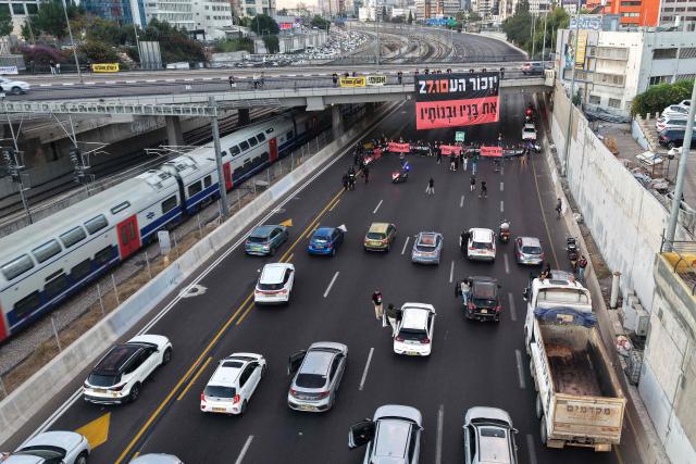 This aerial view shows Israelis holding banners reading 'Remember and never forget' as they block the highway to conduct a moment of silence as part of a memorial ceremony in Tel Aviv on October 7, 2026, to mark the third anniversary of Hamas's October 7 attack. Israel marked the third anniversary of Hamas's October 7 attack with silent tributes, new strikes on Gaza and intense political debate, weeks before elections in which the country's deadliest day will be front and centre. (Photo by Jack GUEZ / AFP)