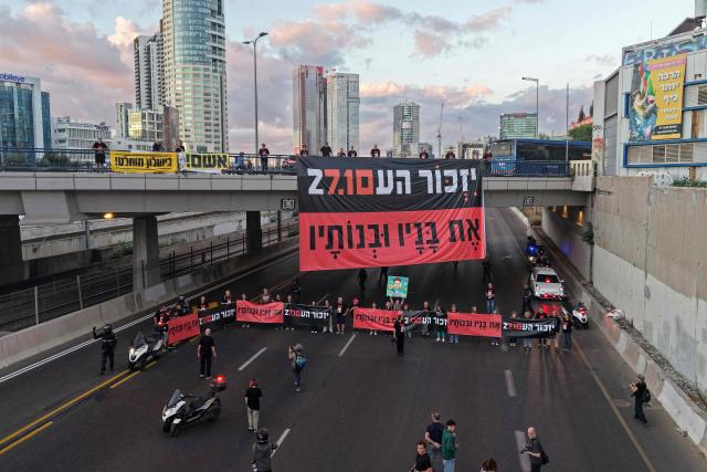 This aerial view shows Israelis holding banners reading 'Remember and never forget' as they block the highway to conduct a moment of silence as part of a memorial ceremony in Tel Aviv on October 7, 2026, to mark the third anniversary of Hamas's October 7 attack. Israel marked the third anniversary of Hamas's October 7 attack with silent tributes, new strikes on Gaza and intense political debate, weeks before elections in which the country's deadliest day will be front and centre. (Photo by Jack GUEZ / AFP)