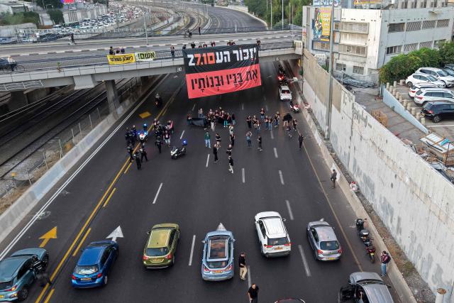 This aerial view shows Israelis holding banners reading 'Remember and never forget' as they block the highway to conduct a moment of silence as part of a memorial ceremony in Tel Aviv on October 7, 2026, to mark the third anniversary of Hamas's October 7 attack. Israel marked the third anniversary of Hamas's October 7 attack with silent tributes, new strikes on Gaza and intense political debate, weeks before elections in which the country's deadliest day will be front and centre. (Photo by Jack GUEZ / AFP)