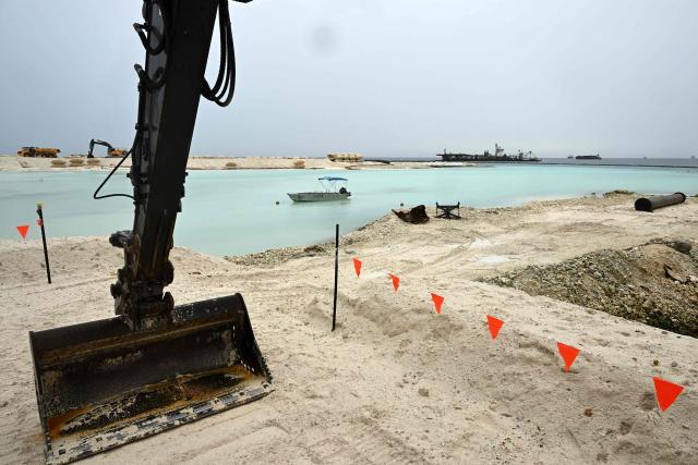 This photo taken on October 6, 2026 shows heavy earthmoving machinery depositing sand at a land reclamation site in Funafuti, Tuvalu. Tuvalu is expanding adaptation measures, including land reclamation and coastal protection works, as rising sea levels linked to climate change threaten the future of the low-lying Pacific island nation. (Photo by Saeed KHAN / POOL / AFP)