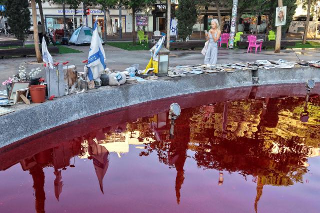 A woman walks around the Dizengoff Fountain, filled with red dye in the Israeli coastal city of Tel Aviv on October 7, 2026, to mark the third anniversary of Hamas's October 7 attack. Israel marked the third anniversary of Hamas's October 7 attack with silent tributes, new strikes on Gaza and intense political debate, weeks before elections in which the country's deadliest day will be front and centre. (Photo by Jack GUEZ / AFP)