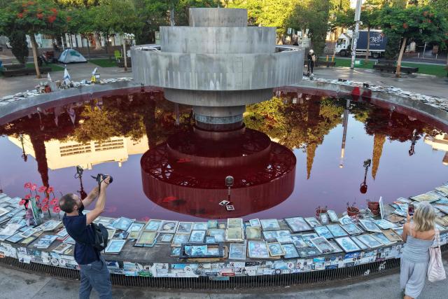 People take pictures of the Dizengoff Fountain, filled with red dye in the Israeli coastal city of Tel Aviv on October 7, 2026, to mark the third anniversary of Hamas's October 7 attack. Israel marked the third anniversary of Hamas's October 7 attack with silent tributes, new strikes on Gaza and intense political debate, weeks before elections in which the country's deadliest day will be front and centre. (Photo by Jack GUEZ / AFP)