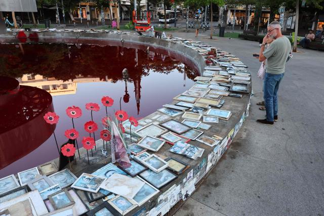 People stand next to the Dizengoff Fountain, filled with red dye in the Israeli coastal city of Tel Aviv on October 7, 2026, to mark the third anniversary of Hamas's October 7 attack. Israel marked the third anniversary of Hamas's October 7 attack with silent tributes, new strikes on Gaza and intense political debate, weeks before elections in which the country's deadliest day will be front and centre. (Photo by Jack GUEZ / AFP)