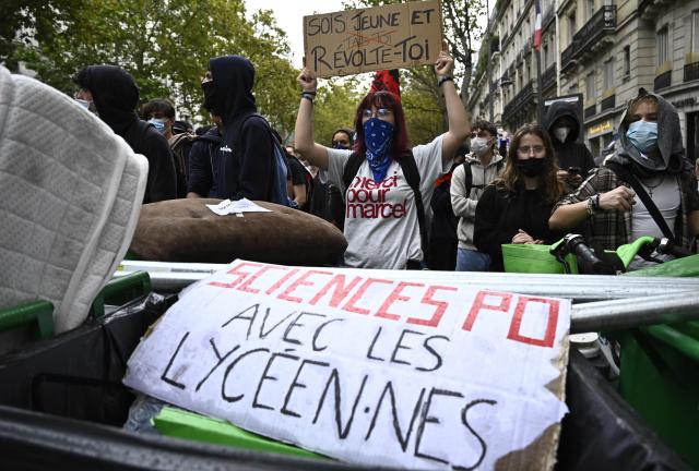 A protester holds a placard reading "be young and revolt" next to another reading "Sciences Po with high-school students" during a demonstration in solidarity with high-school students near Sciences Politiques (Paris Institute of Political Studies) university as part of a nationwide protest movement over learning conditions in Paris, on October 7, 2026. Since late September, pupils have barred the entrances to hundreds of schools, complaining of teacher absences, overloaded timetables, dilapidated classrooms and buildings ill-adapted to rising temperatures, among other grievances. (Photo by JULIEN DE ROSA / AFP)