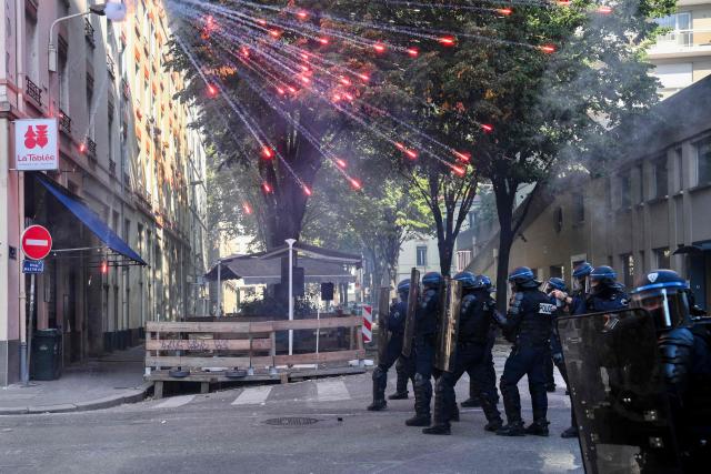 TOPSHOT - Riot police officers stand as fireworks go off above them during a demonstration by high-school students alongside a teachers' union in Lyon, central-eastern France, on October 6, 2026. Since late September, pupils have barred the entrances to hundreds of schools, complaining of teacher absences, overloaded timetables, dilapidated classrooms and buildings ill-adapted to rising temperatures, among other grievances. (Photo by OLIVIER CHASSIGNOLE / AFP)