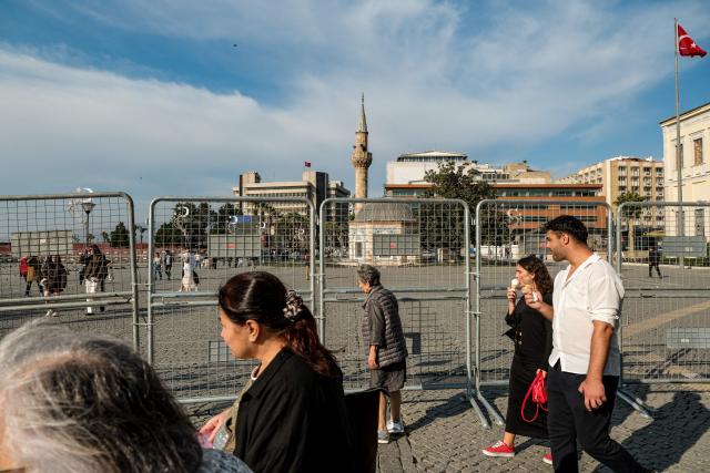 Pedestrians walk past police fences as Turkish Police block Konak square due to potential protests after Izmir mayor joined the ruling Justice and Development Party (AKP) in Izmir, on October 7, 2026. The mayor of Izmir, Turkey's third city and an opposition stronghold, on Wednesday defected to the ruling AKP, in a huge symbolic victory for Turkish President Recep Tayyip Erdogan. Mayor Cemil Tugay's decision to join the Islamic-rooted Justice and Development Party (AKP) was announced by Erdogan at a parliamentary group meeting in Ankara where he personally welcomed the mayor in a party-like atmosphere broadcast live on TV. (Photo by Murat Kocabas / AFP)